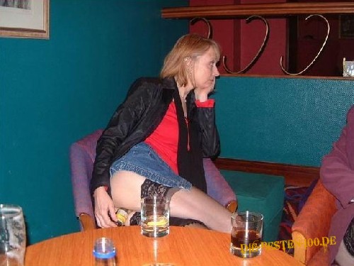 Frau schiebt sich Bierflasche in einer Kneipe zwischen Ihre Beine